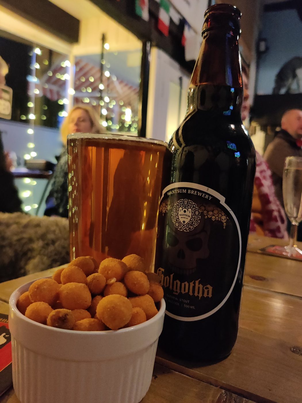 A bottle and a pint with a bowl of snacks